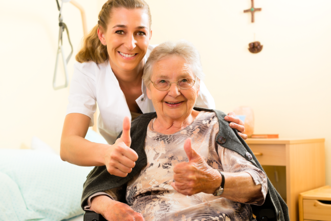 caregiver and elder patient smiling while showing thumbs up